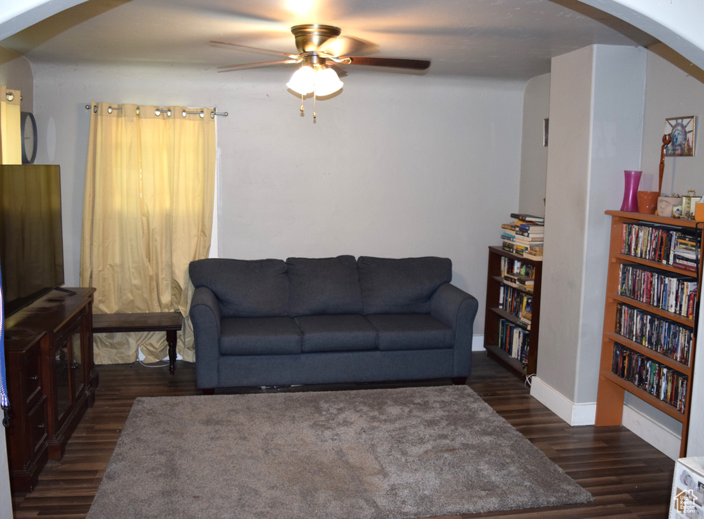 Living room featuring arched walkways, ceiling fan, dark wood-style floors, and baseboards