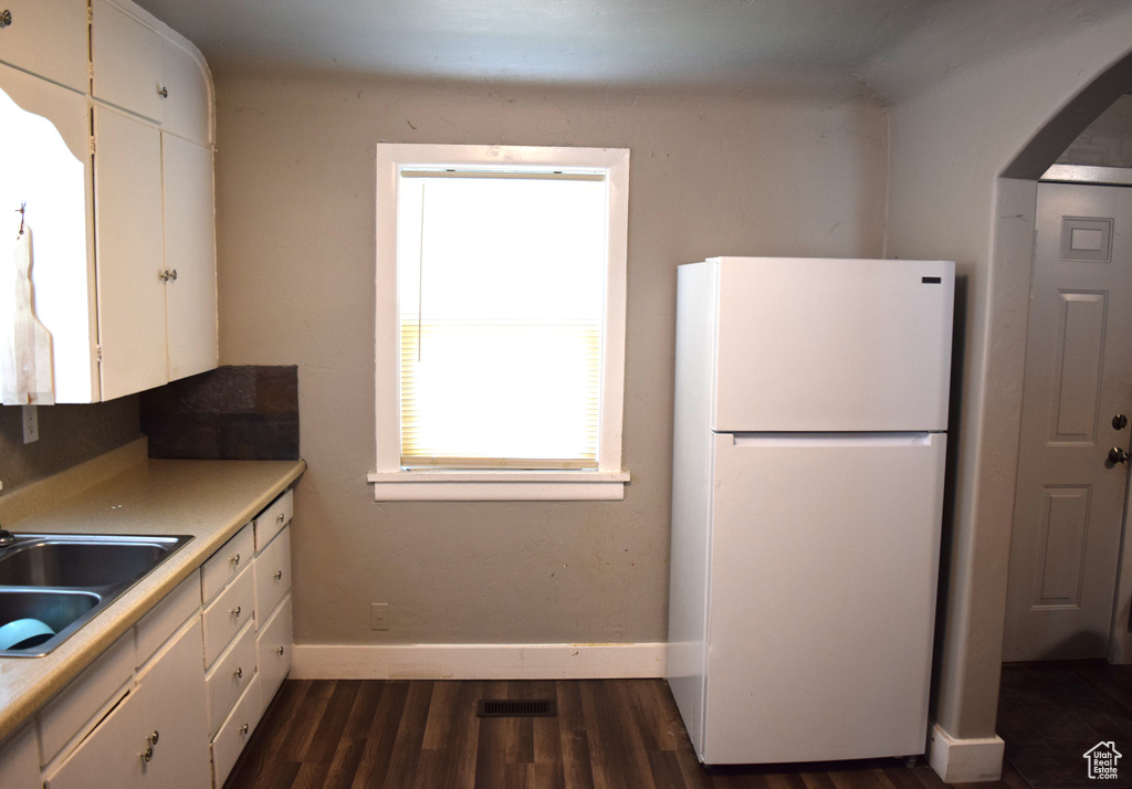 Kitchen with freestanding refrigerator, a sink, white cabinets, dark wood finished floors, and baseboards