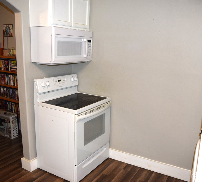 Kitchen featuring white appliances, baseboards, dark wood-type flooring, and white cabinets