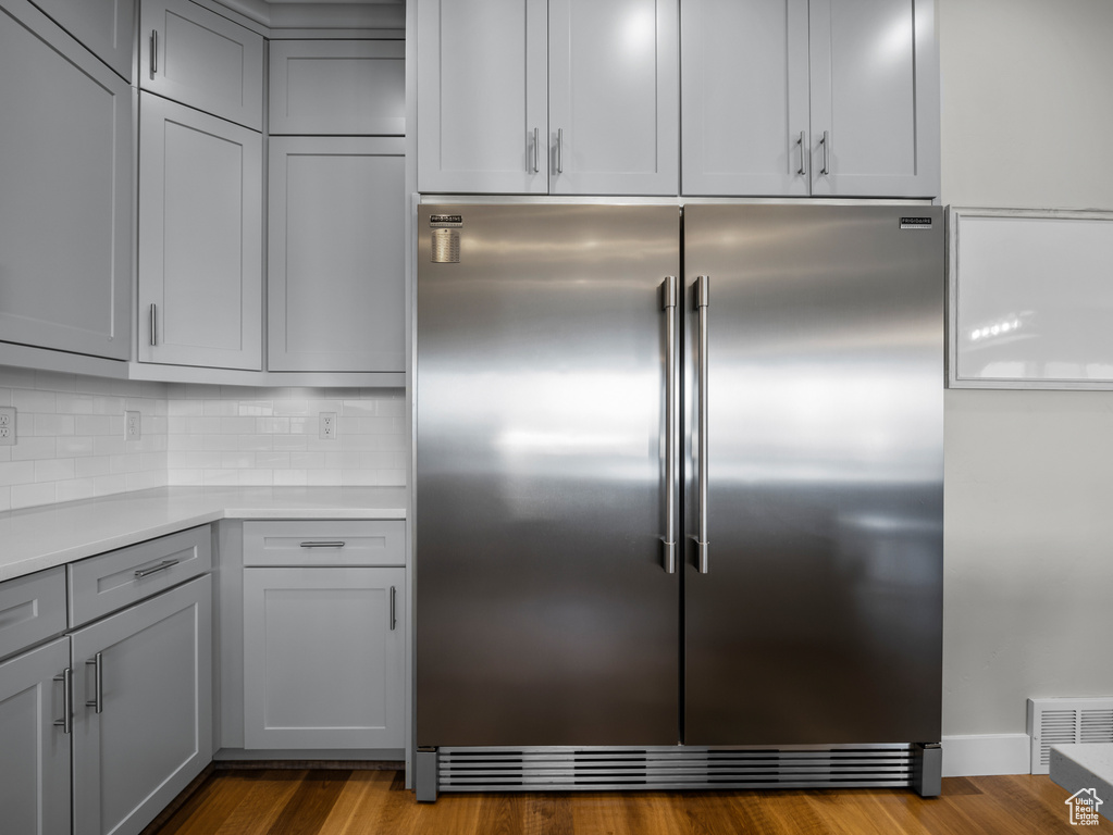 Kitchen featuring stainless steel built in fridge, gray cabinetry, backsplash, light countertops, and dark wood-style flooring