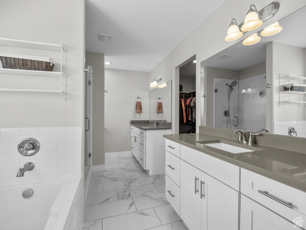 Bathroom featuring a shower stall, marble finish flooring, two vanities, a spacious closet, and a garden tub