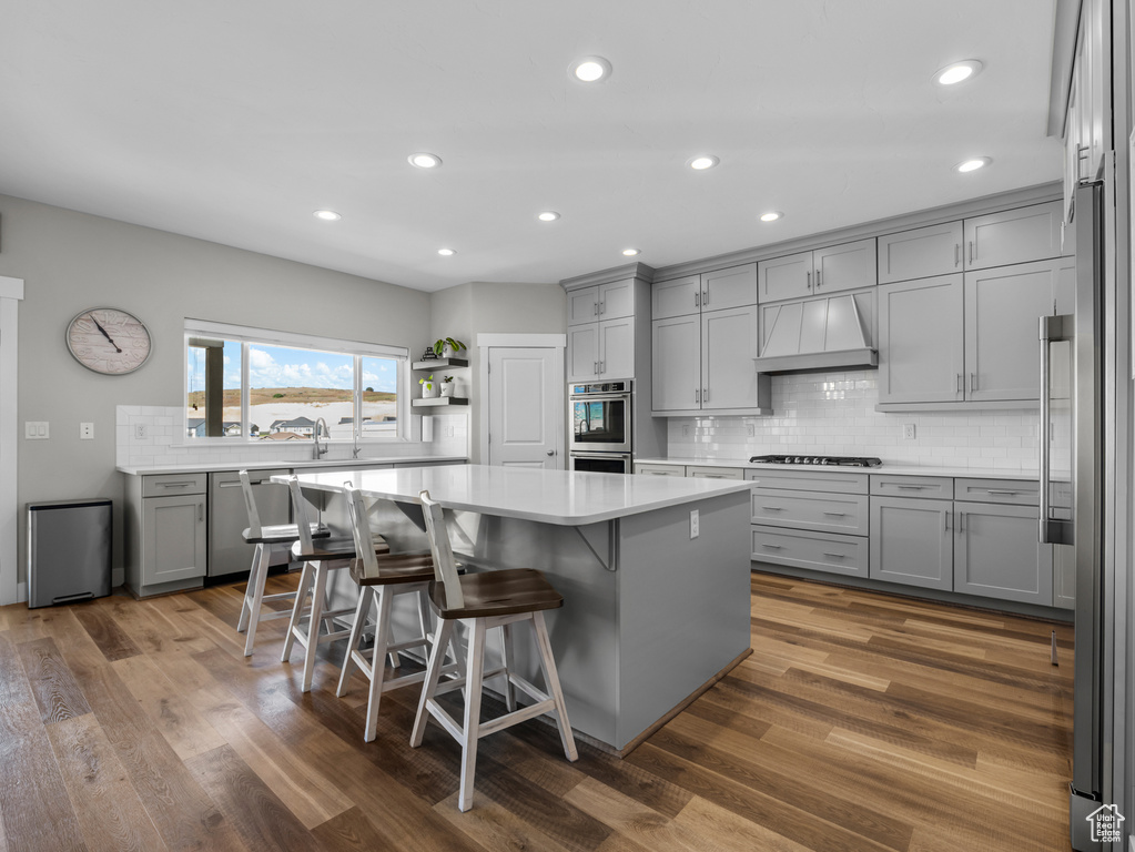 Kitchen with gray cabinetry, custom range hood, appliances with stainless steel finishes, backsplash, and a center island