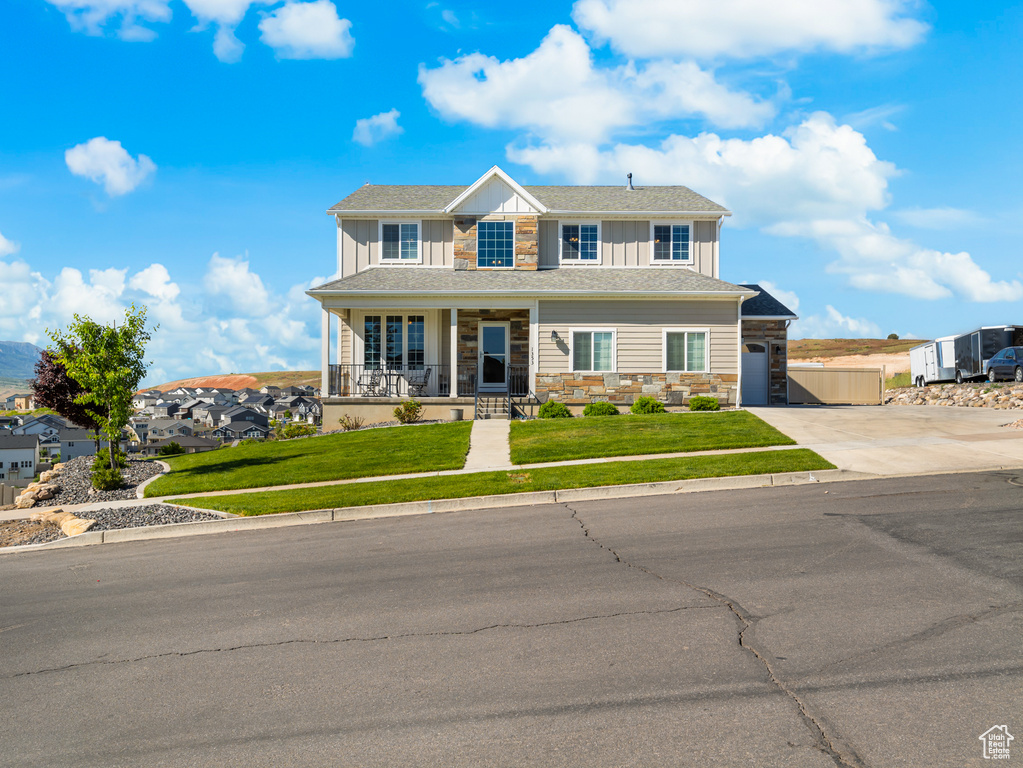View of front of house featuring stone siding, a porch, board and batten siding, concrete driveway, and a front yard