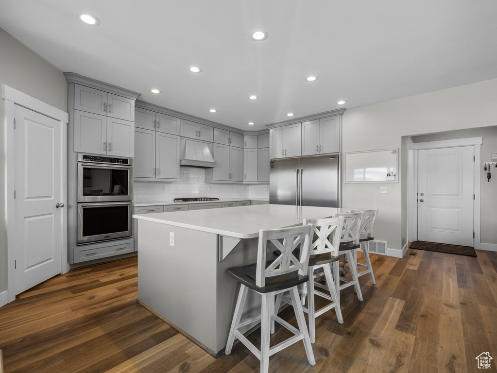 Kitchen featuring appliances with stainless steel finishes, gray cabinetry, custom exhaust hood, light countertops, and dark wood-style floors