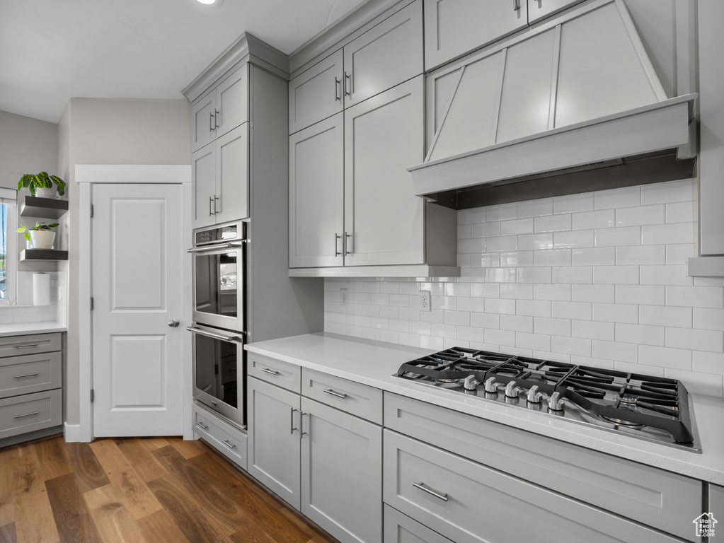 Kitchen with gray cabinetry, appliances with stainless steel finishes, custom range hood, and backsplash