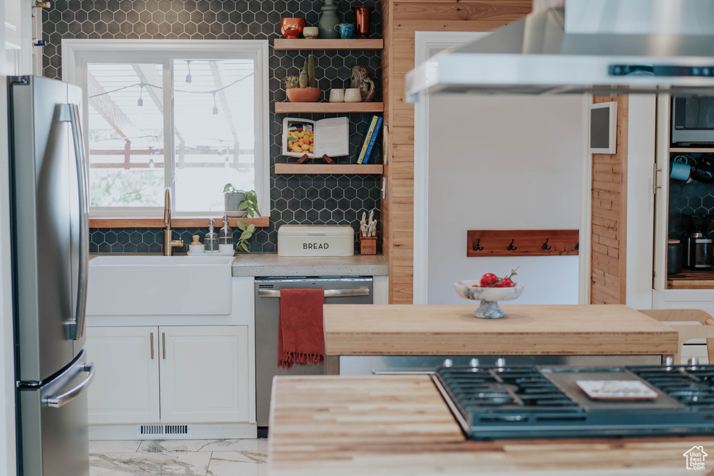 Kitchen with stainless steel appliances, a sink, white cabinetry, exhaust hood, and light countertops