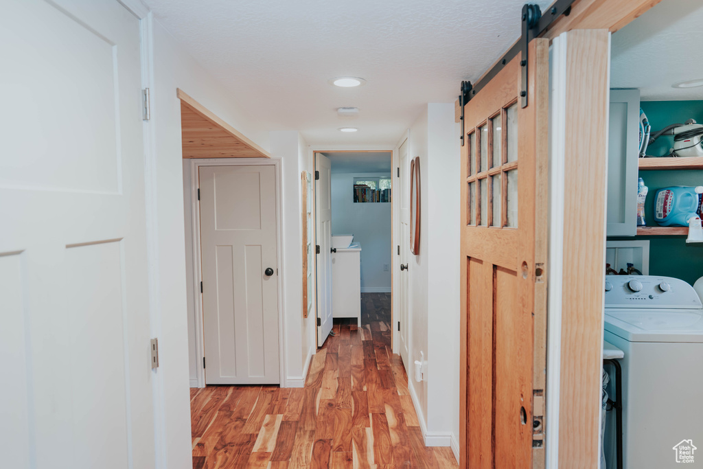 Hall with washer / clothes dryer, a barn door, and light wood-style floors