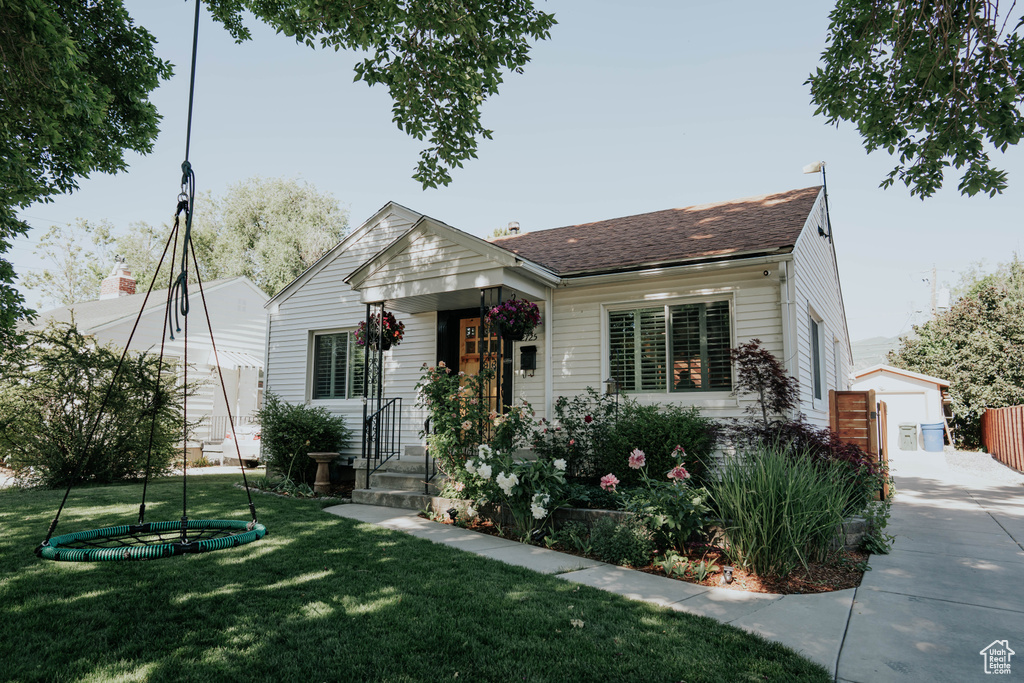 Bungalow-style home featuring a front yard, an outdoor structure, and a shingled roof