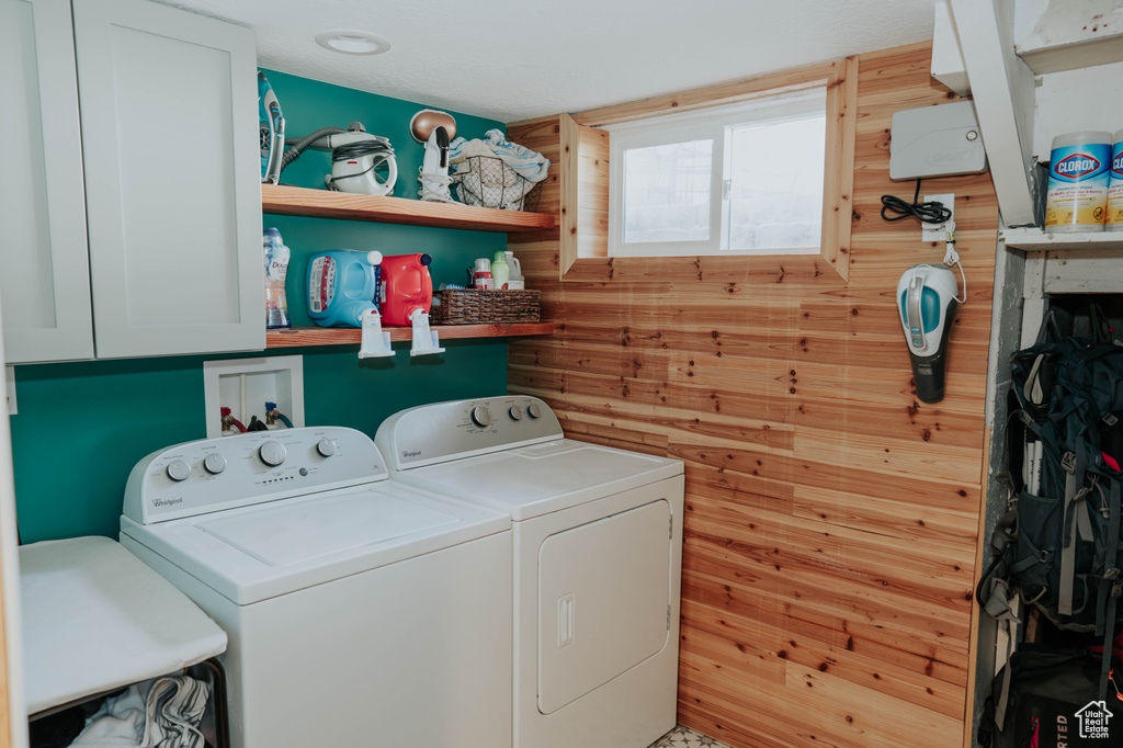 Washroom with independent washer and dryer, wooden walls, and cabinet space