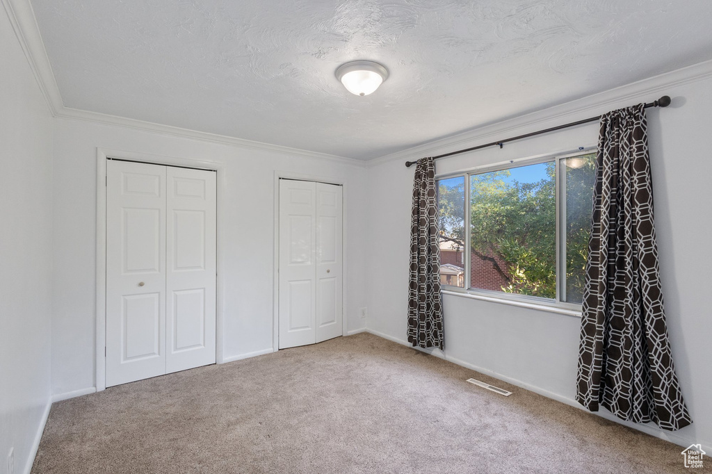 Unfurnished bedroom with multiple closets, carpet flooring, and crown molding