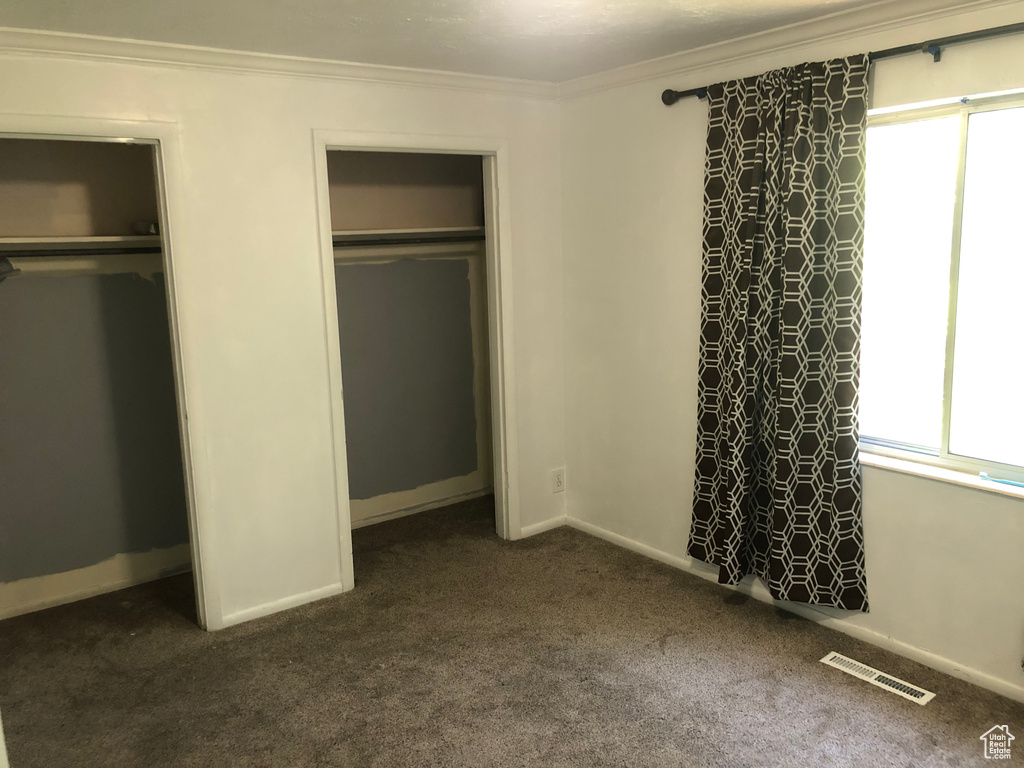 Unfurnished bedroom with dark carpet, two closets, ornamental molding, and baseboards