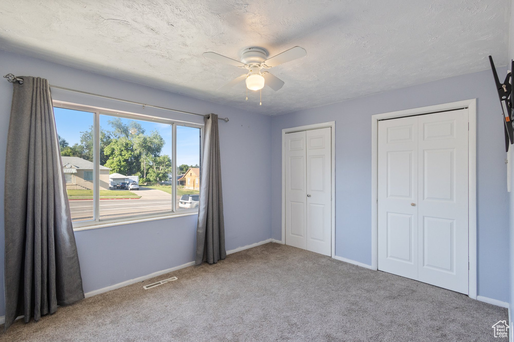 Unfurnished bedroom with carpet, multiple closets, ceiling fan, and a textured ceiling