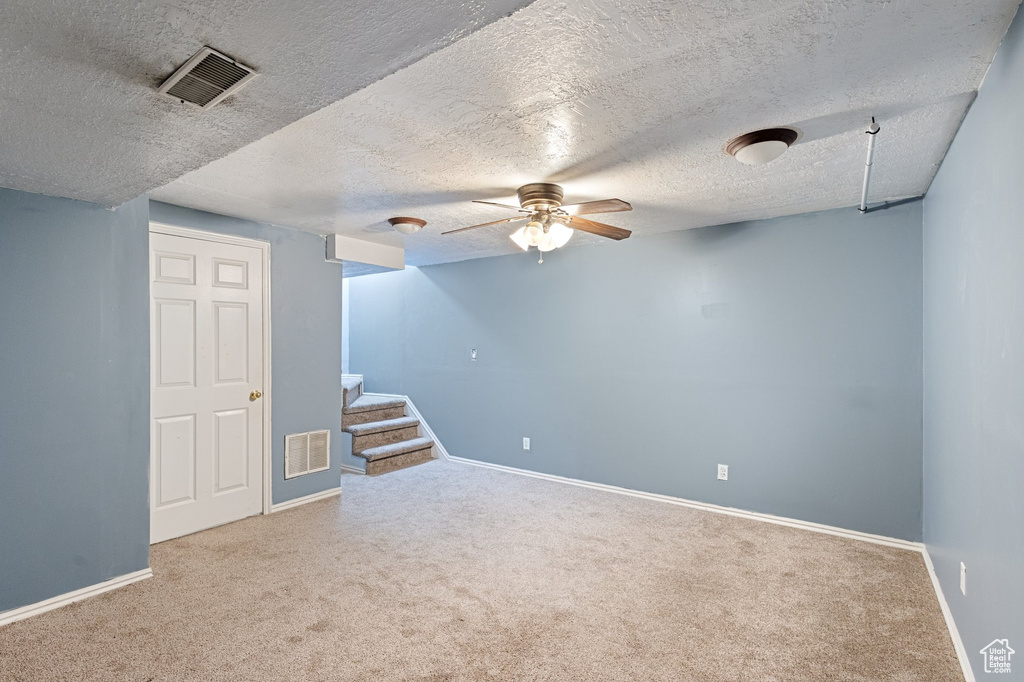 Finished below grade area with carpet floors, ceiling fan, a textured ceiling, and stairway