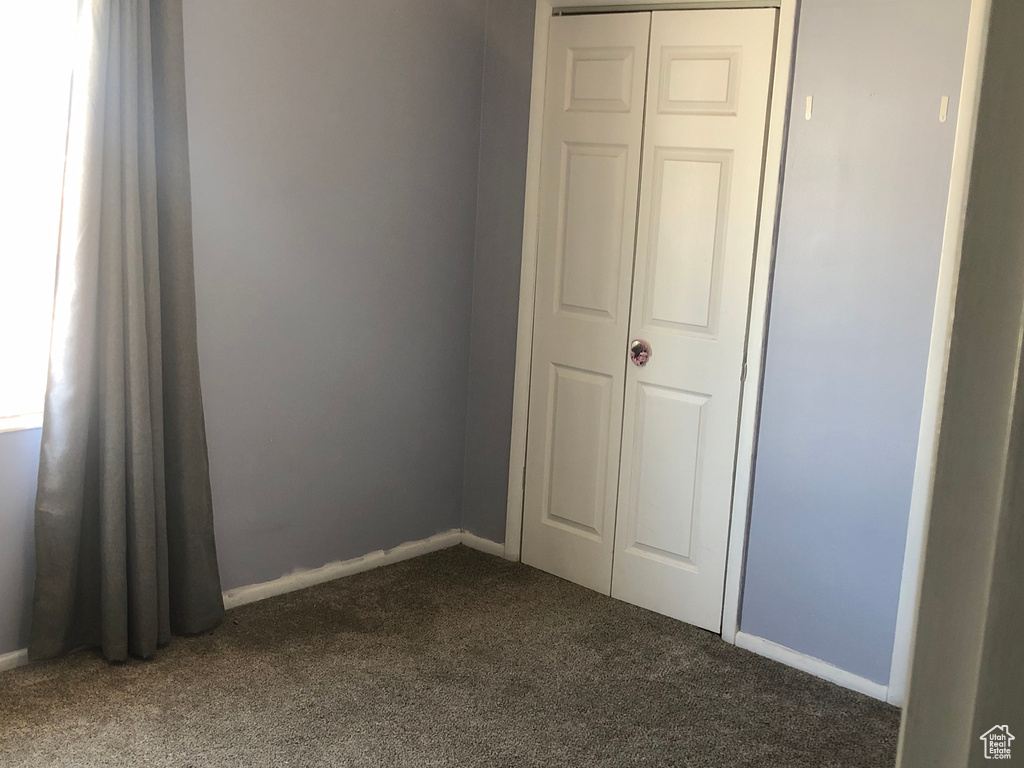 Unfurnished bedroom with dark carpet, baseboards, and a closet