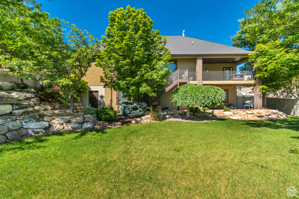 Back of house with a yard, stucco siding, a balcony, and stairway