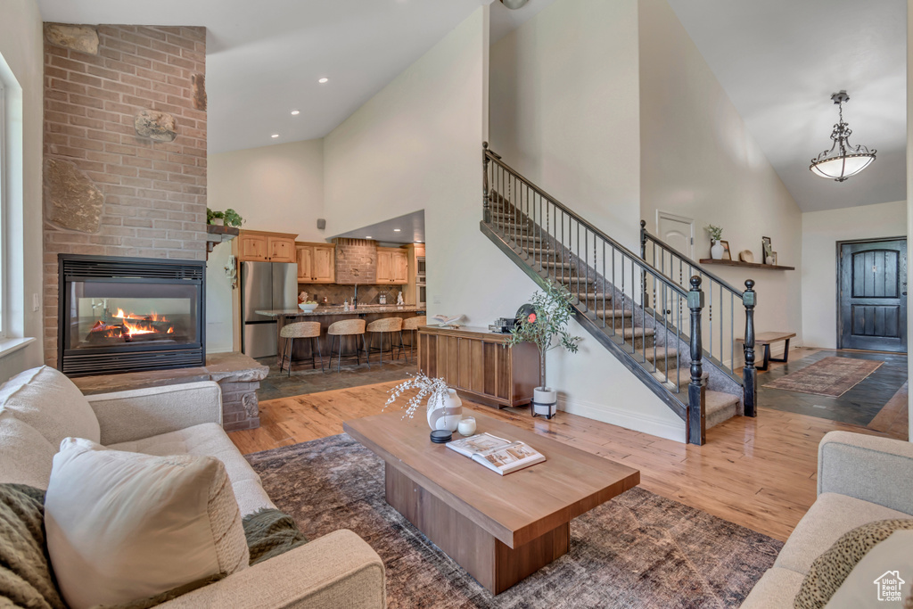 Living room with high vaulted ceiling, light wood-style floors, stairs, a brick fireplace, and baseboards