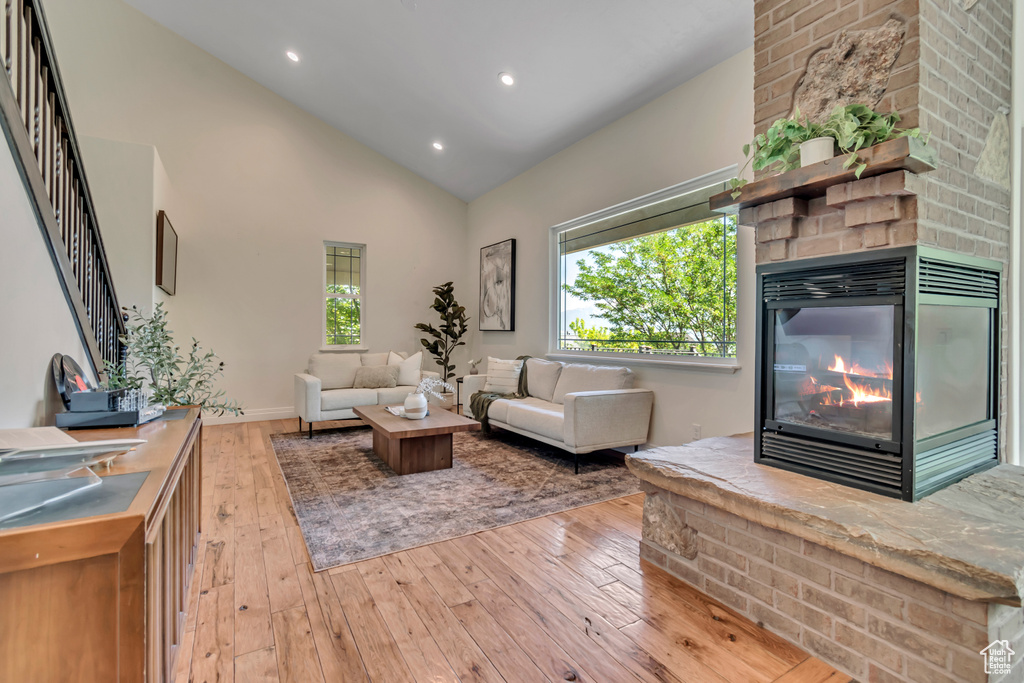 Living area with hardwood / wood-style floors, a fireplace, recessed lighting, high vaulted ceiling, and stairway