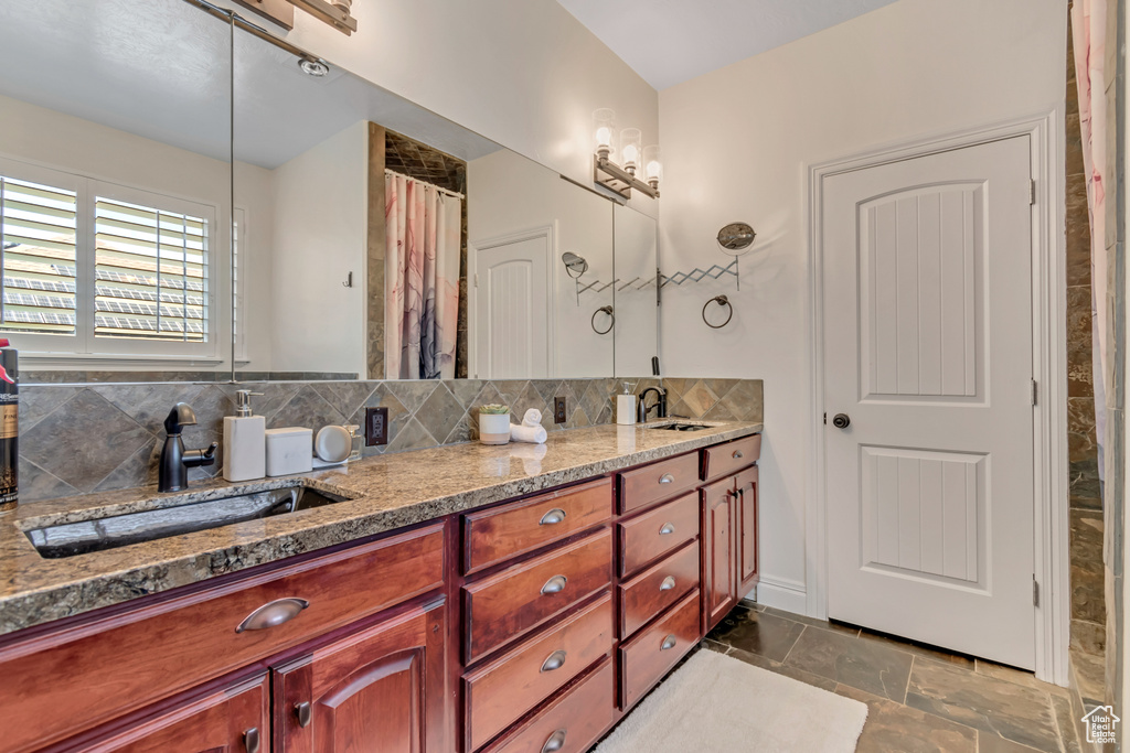 Bathroom featuring double vanity, backsplash, and stone finish floors