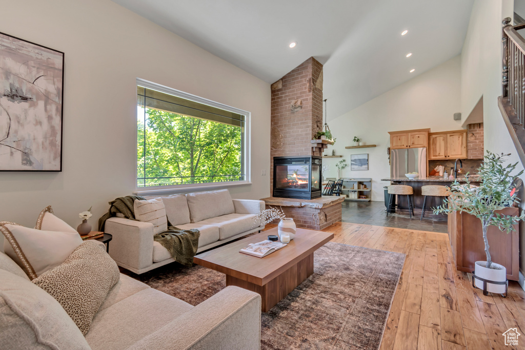 Living area featuring light wood-type flooring, a brick fireplace, recessed lighting, and high vaulted ceiling