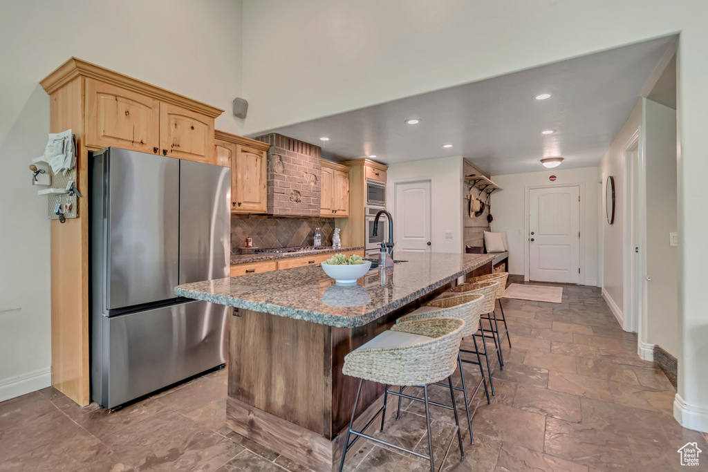 Kitchen featuring appliances with stainless steel finishes, baseboards, a kitchen island with sink, a kitchen breakfast bar, and recessed lighting