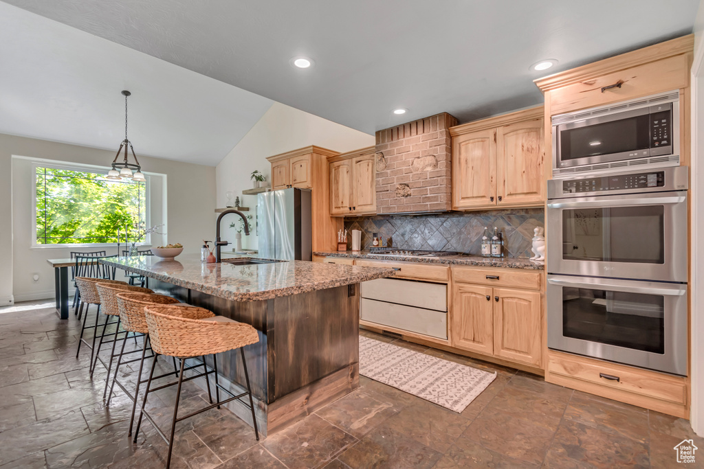 Kitchen with appliances with stainless steel finishes, a sink, vaulted ceiling, decorative backsplash, and a kitchen breakfast bar