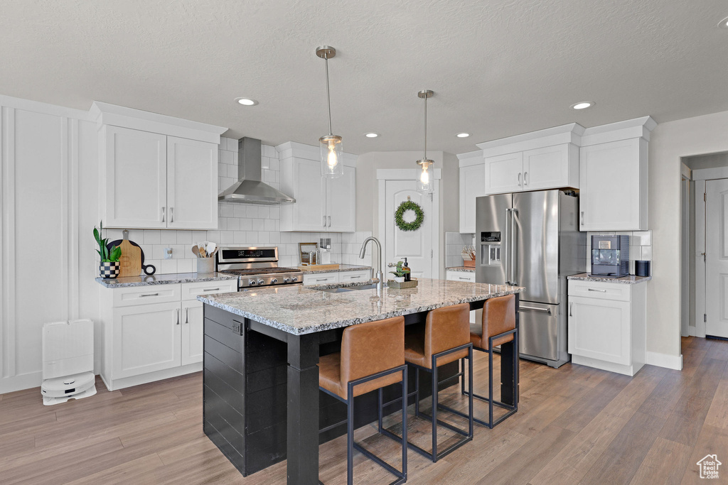 Kitchen with wall chimney exhaust hood, appliances with stainless steel finishes, a sink, decorative backsplash, and a kitchen breakfast bar