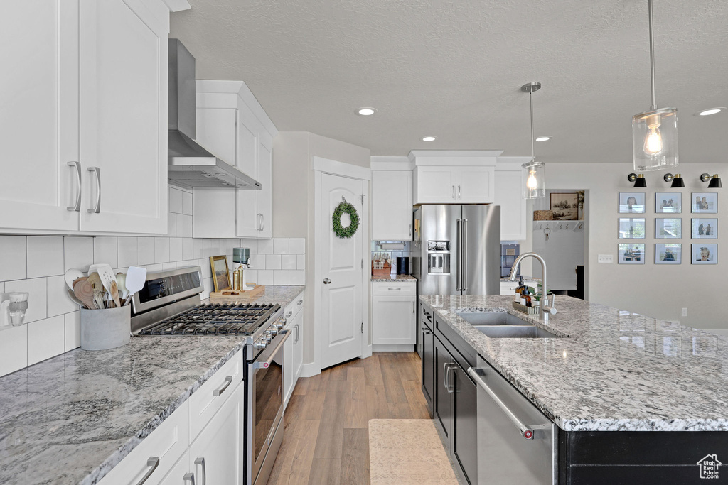 Kitchen featuring wall chimney exhaust hood, appliances with stainless steel finishes, a sink, light wood-type flooring, and white cabinets