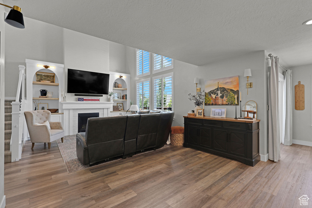 Living room featuring wood finished floors, a fireplace, a textured ceiling, built in shelves, and a high ceiling