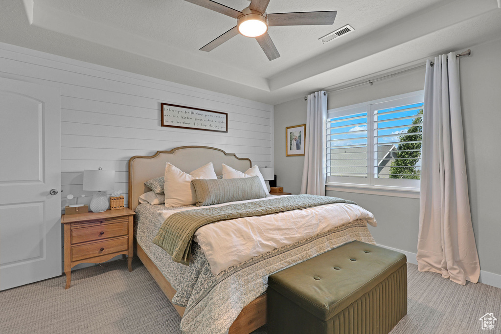 Bedroom featuring light carpet, a raised ceiling, ceiling fan, wood walls, and baseboards