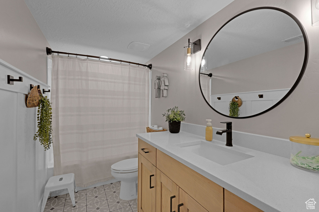 Bathroom with toilet, vanity, a textured ceiling, tile patterned flooring, and shower / bath combo