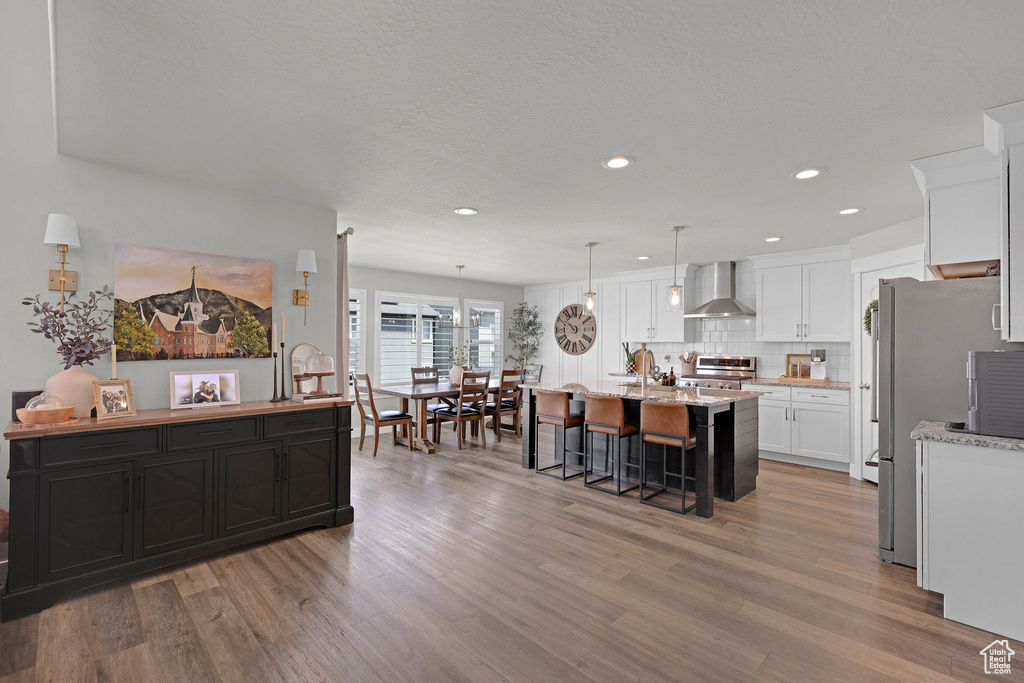 Kitchen featuring stainless steel range oven, wall chimney exhaust hood, freestanding refrigerator, a kitchen island with sink, and light wood-style flooring