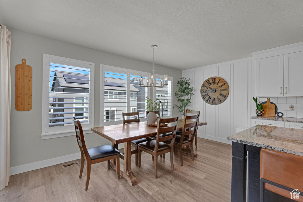 Dining area featuring light wood-style flooring, a chandelier, baseboards, and a textured ceiling