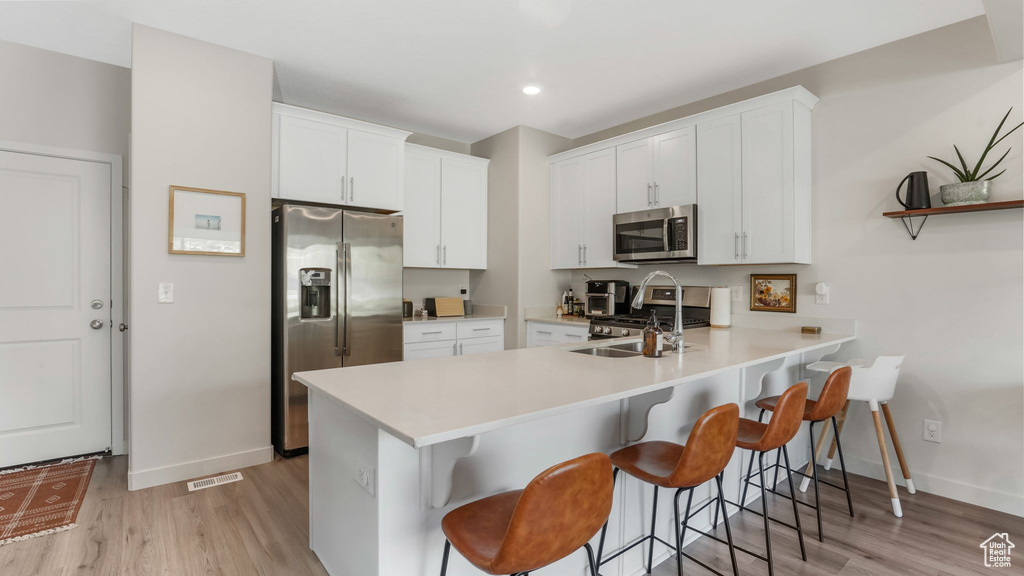 Kitchen with stainless steel appliances, light wood finished floors, baseboards, a peninsula, and recessed lighting