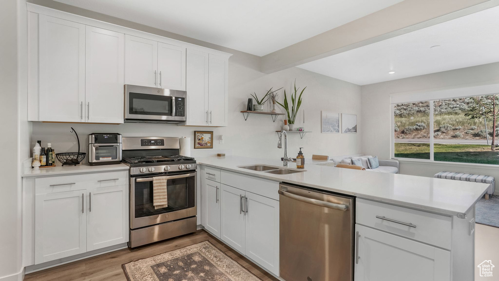 Kitchen featuring stainless steel appliances, a sink, a peninsula, light wood-type flooring, and light countertops