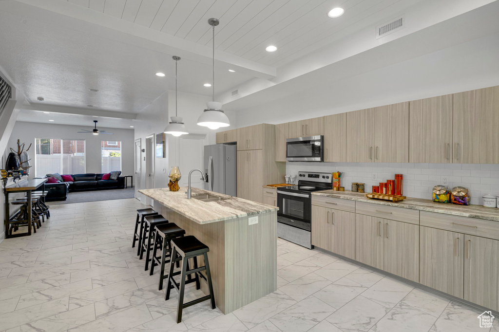Kitchen with appliances with stainless steel finishes, light marble finish floors, a breakfast bar area, light brown cabinetry, and recessed lighting