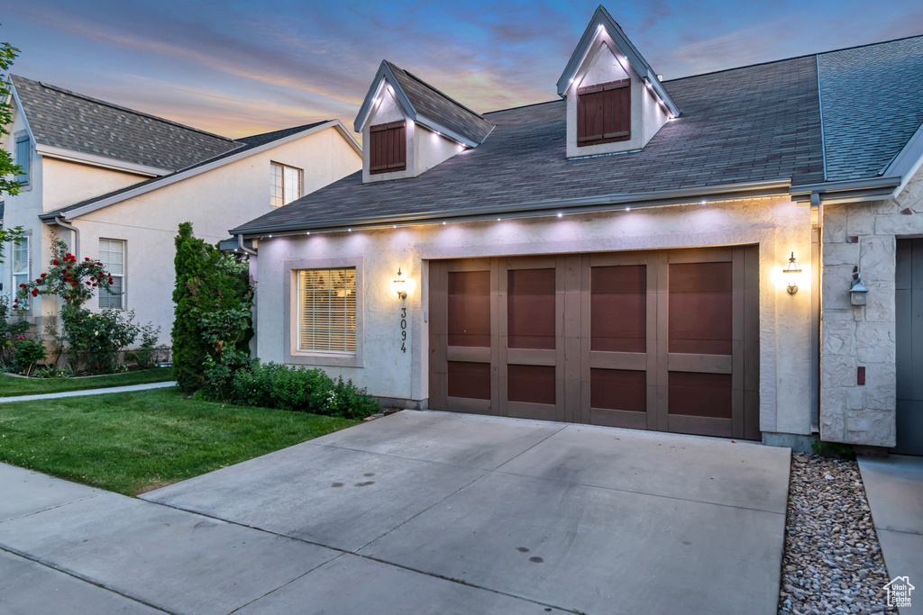 View of front facade featuring driveway, a yard, stucco siding, an attached garage, and a shingled roof
