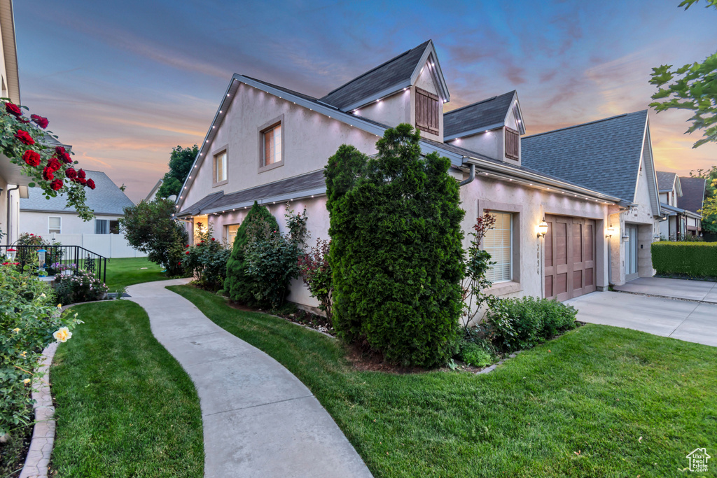 Property exterior at dusk featuring driveway, stucco siding, a lawn, and a garage