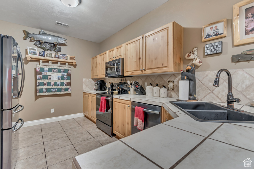 Kitchen with stainless steel appliances, a sink, light brown cabinets, decorative backsplash, and light tile patterned floors