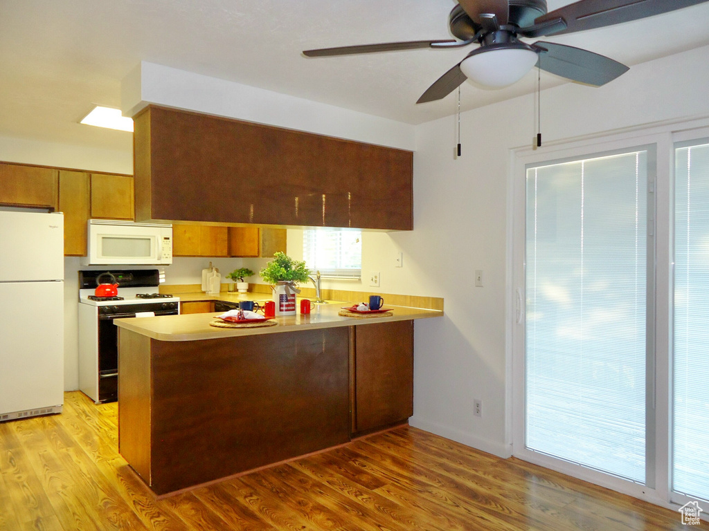 Kitchen with white appliances, a peninsula, brown cabinetry, a ceiling fan, and light wood-type flooring