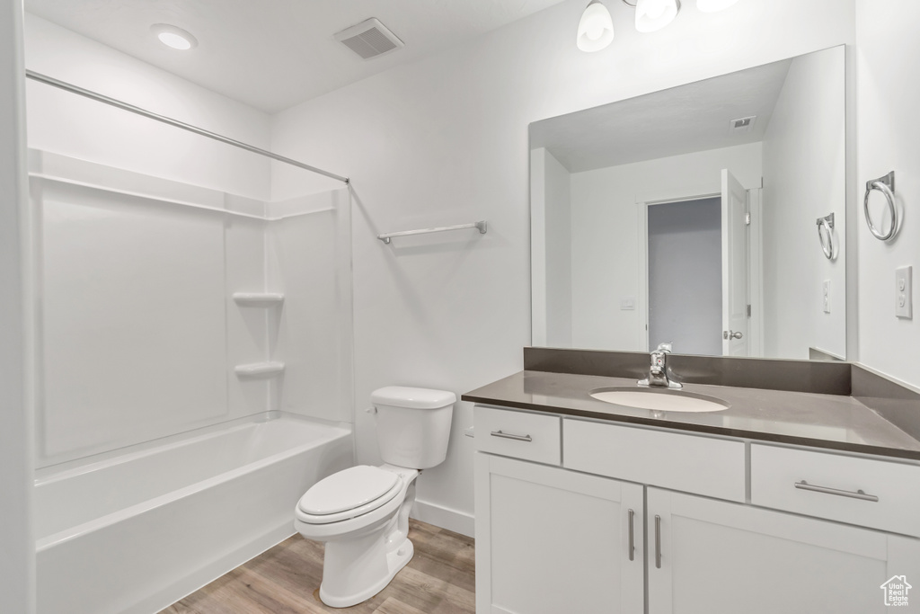 Bathroom with wood finished floors, toilet, vanity, shower / bathtub combination, and baseboards