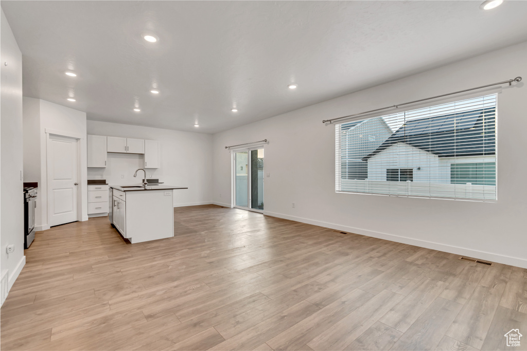 Kitchen featuring dark countertops, a sink, recessed lighting, baseboards, and light wood-style flooring