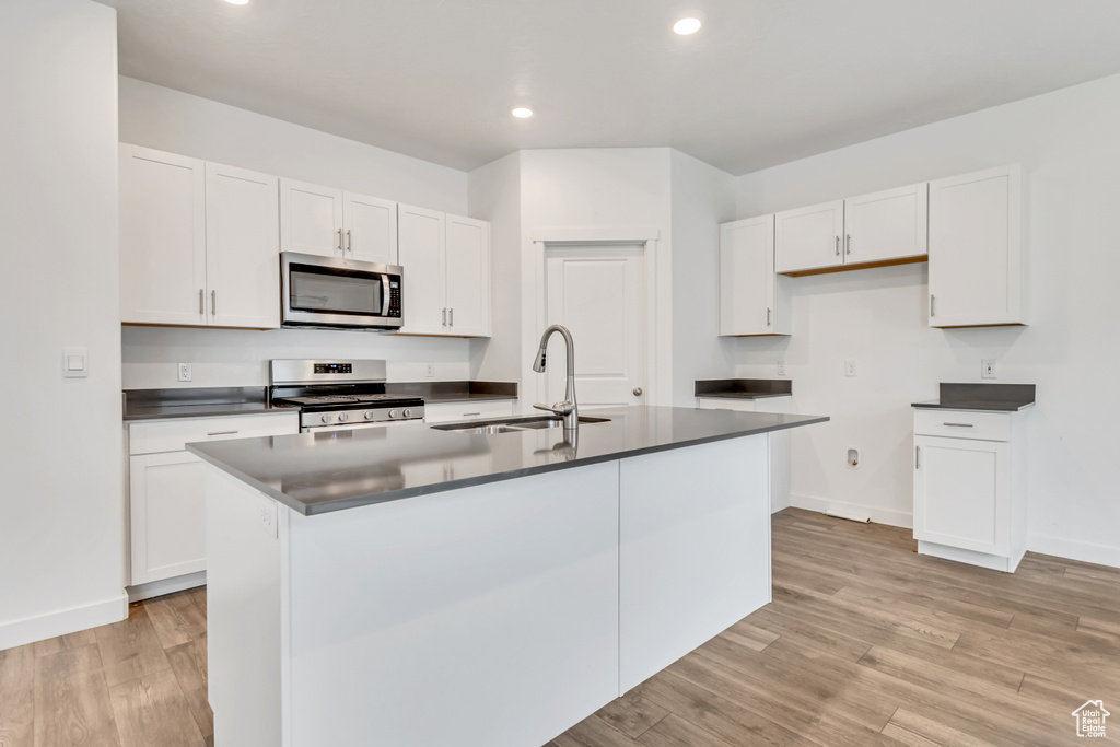 Kitchen featuring stainless steel appliances, a sink, dark countertops, white cabinetry, and light wood-style floors