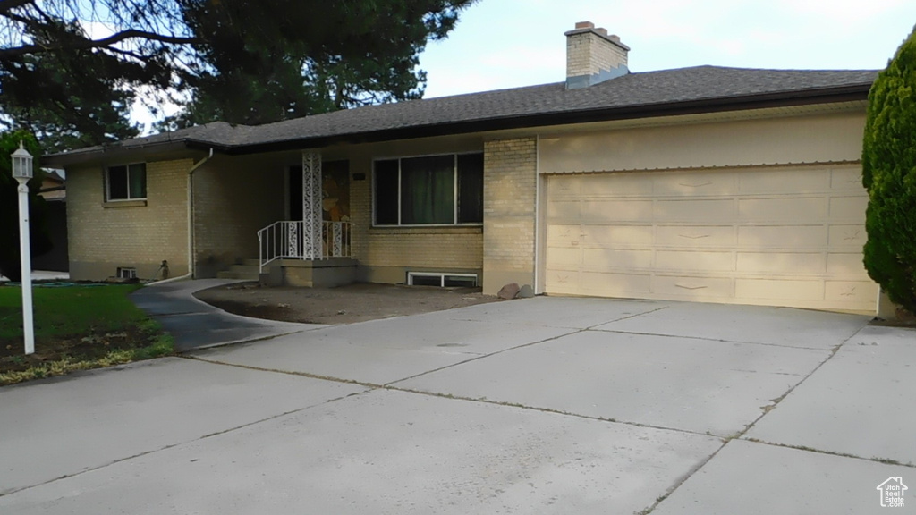 Single story home featuring brick siding, concrete driveway, a garage, and a chimney