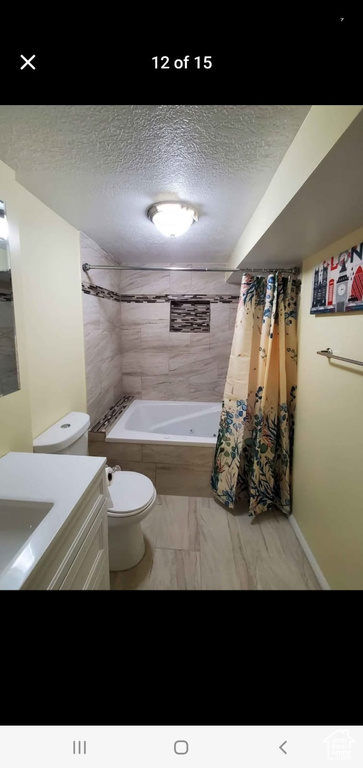 Bathroom featuring a textured ceiling, toilet, vanity, shower / bath combo, and marble look tiles