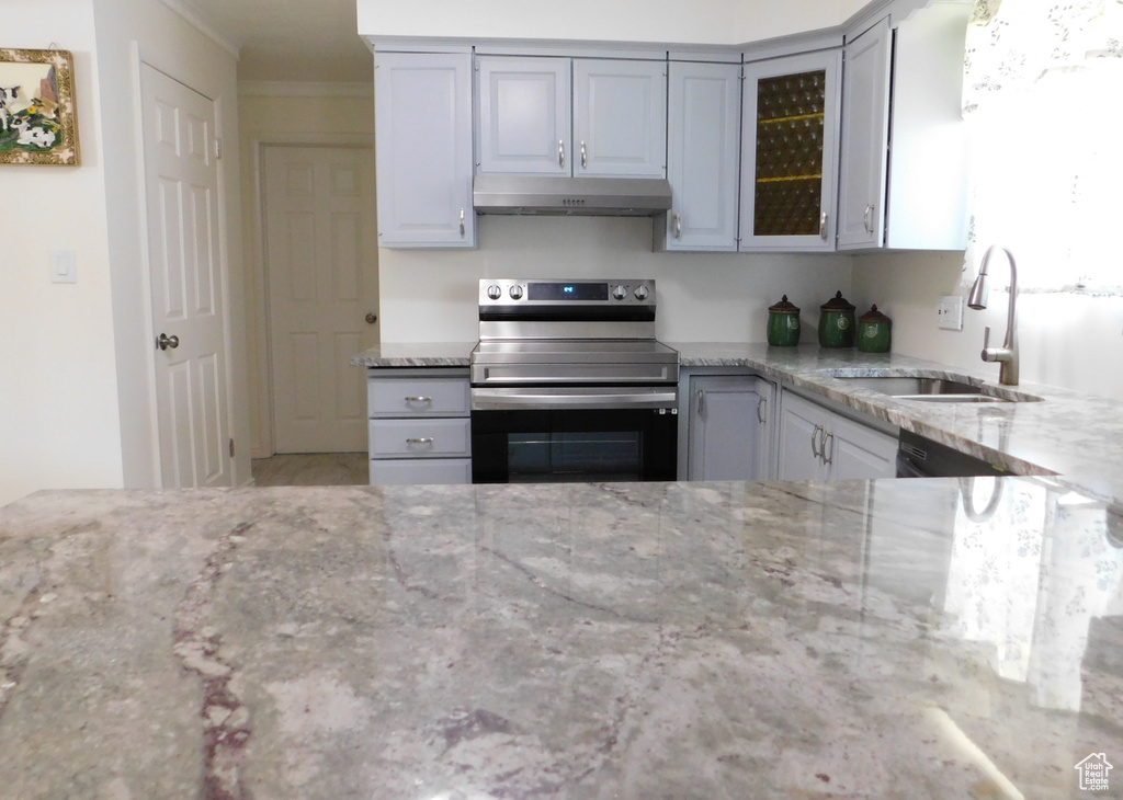 Kitchen with electric stove, under cabinet range hood, a sink, light stone countertops, and glass insert cabinets