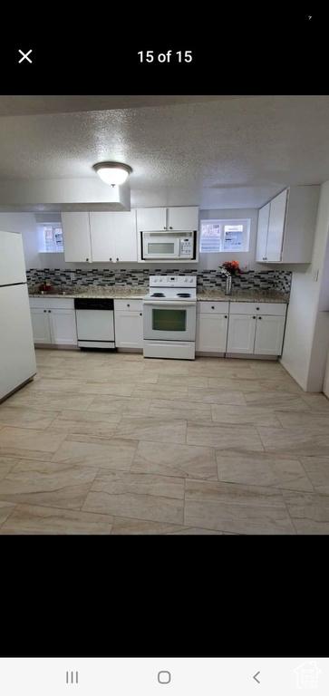 Kitchen featuring white appliances, white cabinetry, and a textured ceiling