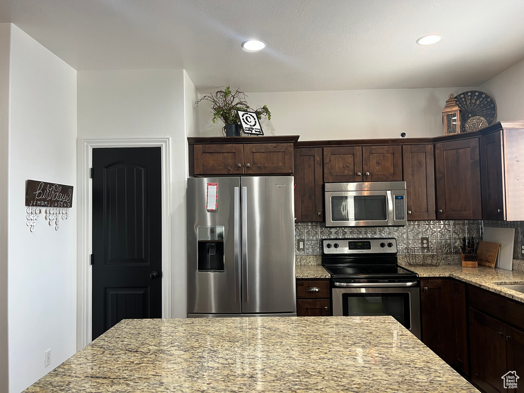 Kitchen with appliances with stainless steel finishes, light stone countertops, decorative backsplash, dark brown cabinets, and recessed lighting