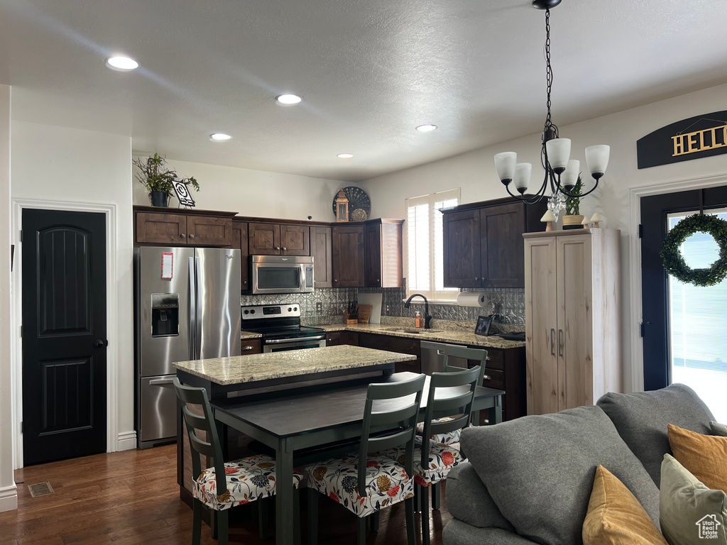 Kitchen featuring appliances with stainless steel finishes, a sink, a chandelier, dark brown cabinetry, and backsplash