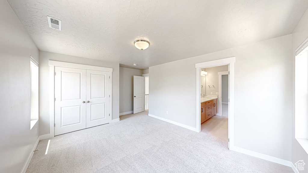 Unfurnished bedroom with baseboards, light carpet, a closet, a textured ceiling, and connected bathroom