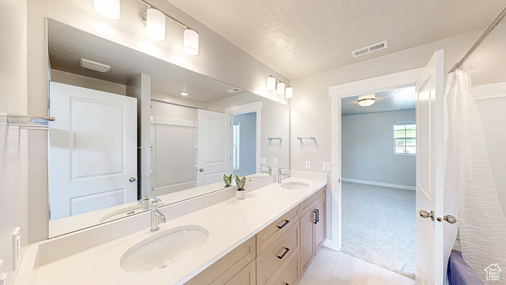 Bathroom featuring a textured ceiling, double vanity, tile patterned floors, and baseboards